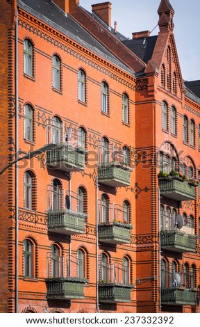 Red facade of the brick wall of the european-style building with windows and green balconies