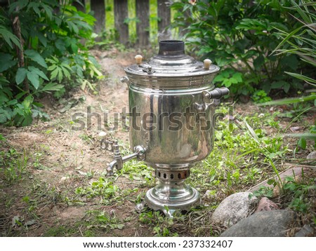 Smoking russian samovar standing on the ground in sunny summer garden
