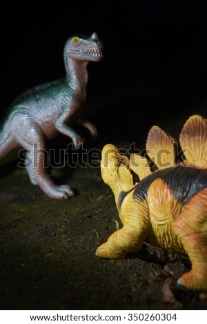 Toy dinosaur figurine in a real nature scenery outdoors. Two dinosaurs fighting