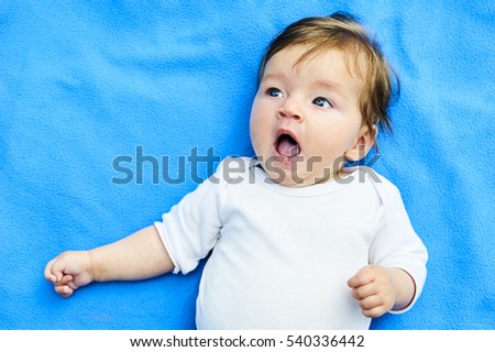 Newborn girl with blue eyes in the beautiful park outdoors, lies on a blue blanket and yawning.