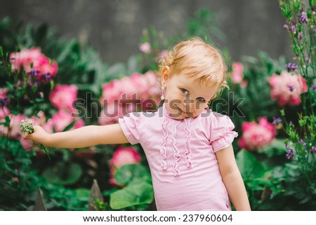 the little girl with white hair and blue eyes in a pink t-shirt poses against flowers