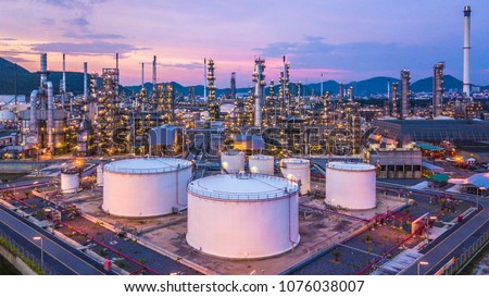 Aerial top view oil and gas chemical tank with oil refinery factory background at twilight.