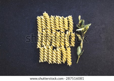 Vintage food background: Spiral pasta on a dark cloth background with a sprig of herbs. Top view