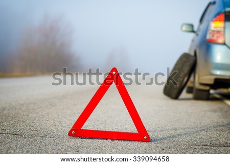 Emergency stop sign. Blue car punctured tire. Empty road in a foggy day