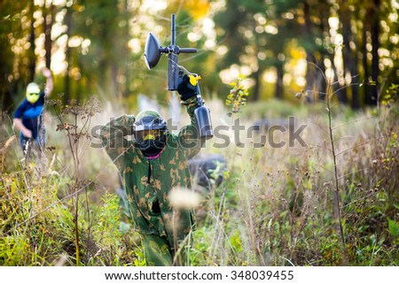 Paintball sport player in protective uniform and mask playing with gun outdoors. Getting in mask.