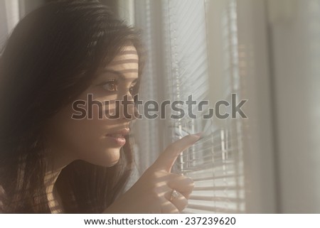Girl spies through the window blinds