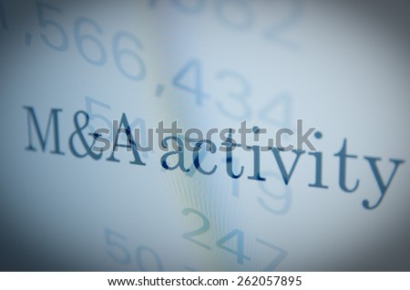 Inscription M&A (Mergers and acquisitions) activity on a PC monitor. Financial data as background. Multiple exposure.