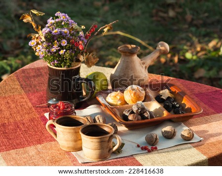 Beautiful autumn still life composition with bright bouquet of natural flowers, coffee, cherry jam, green pear, chocolate candies and profiteroles outdoors