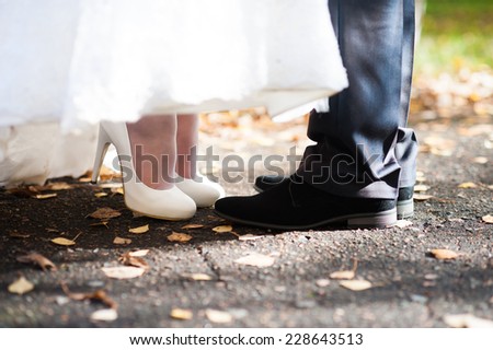 Close view of bride and groom\'s feet turned to each other kissing in autumn sunlight outdoors