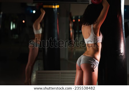 Sexy hot brunette female boxer with perfect butt in shorts posing standing by the punching bag