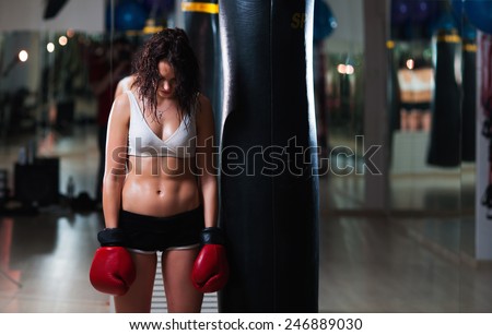 Sexy upset brunette female boxer standing by the punching bag