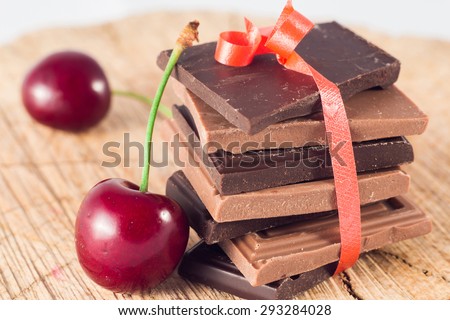 Milk and dark chocolate pyramid with cherry on wooden table.
