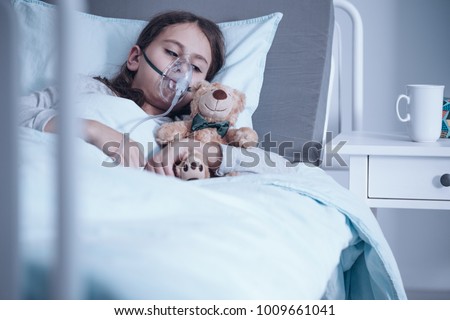 Kid with cystic fibrosis lying in a hospital bed with oxygen mask and plush toy