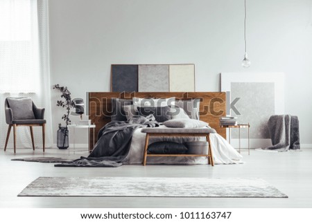 Grey and white bedroom interior with armchair, carpet, bed and painting standing on the floor