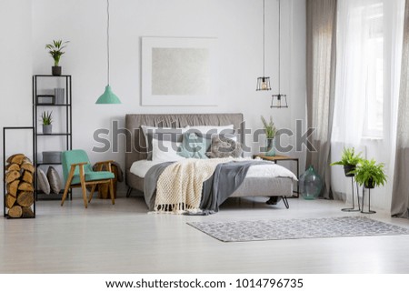 Green lamp above retro chair next to bed against the wall with silver painting in spacious bedroom interior
