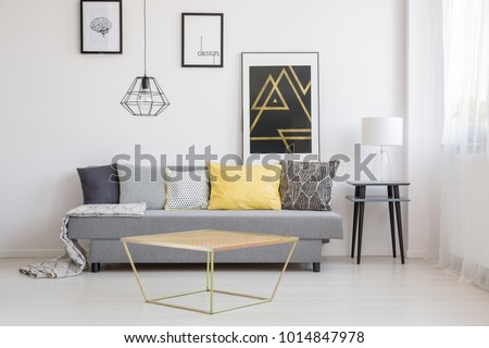 Gold table in front of a gray couch with black, white and yellow cushions in simple living room interior