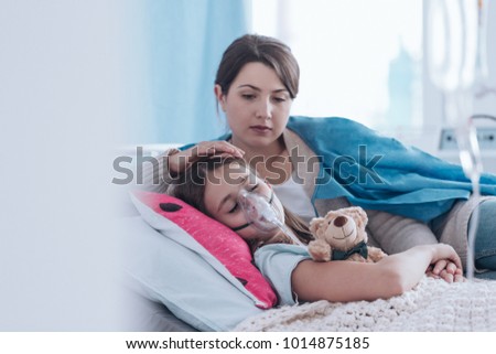Worried mother taking care of a kid with cystic fibrosis lying in hospital bed with plush toy
