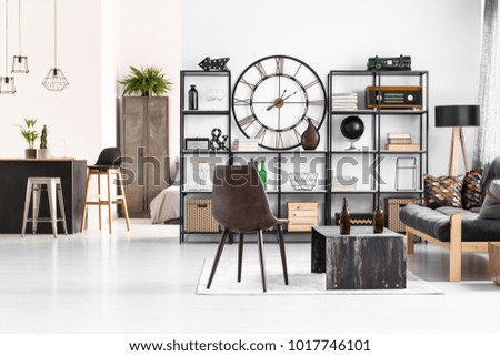 Leather chair standing next to an industrial table with beer bottles on it in manly flat interior with open living room