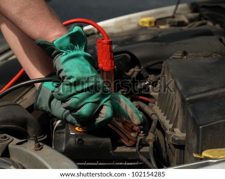 Charging battery in car by mechanic in gloves