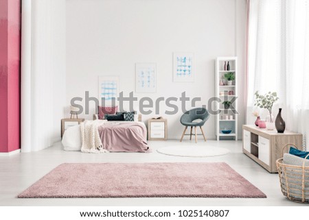 Pink carpet in spacious bedroom interior with grey chair next to bed against the wall with posters