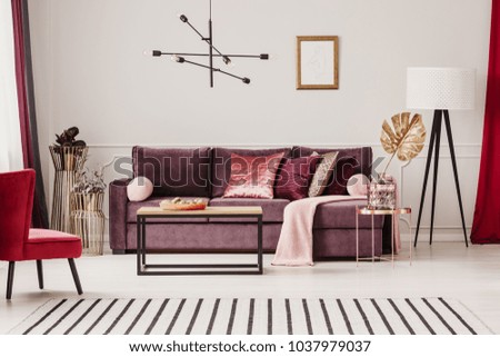 Gold leaf on copper table in sophisticated living room interior with striped carpet and violet sofa