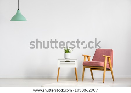 Pink armchair and wooden table on empty wall in simple living room interior
