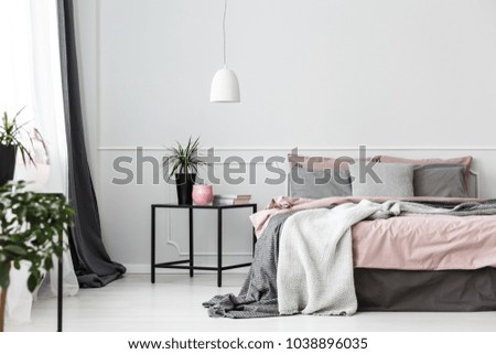 Grey bedsheets on bed in pink bedroom interior with plant on the table against white wall