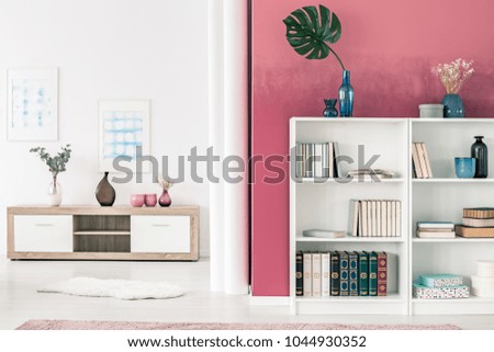 White bookcases and wooden shelf in spacious, white and red living room interior