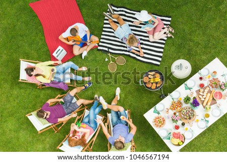 Top view of group of young friends having summer barbecue party in the backyard with grill and table full of delicious food