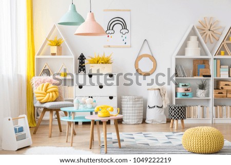 Yellow pouf near pink table with a phone in pastel kid\'s playroom interior with poster on white wall