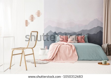 Gold, metal chair in a soft, bright bedroom interior with a mountains wallpaper, pastel pink and blue bedding and pillows