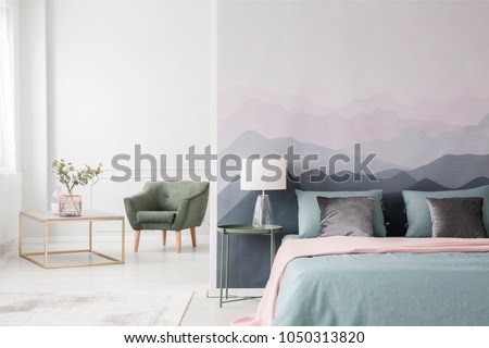 Large bed with blue sheets and a pink blanket by a landscape wallpaper in a cozy, modern bedroom interior