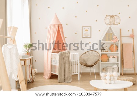 Sweet, spacious nursery room interior for a baby girl with white furniture, pastel pink decorations and golden polka dot wallpaper