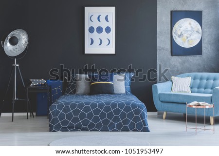 Blue sofa in bedroom interior with navy blue bed against dark wall with gallery of posters