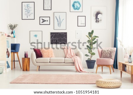 Interior of a pink living room with white couch, pink armchair and posters on the wall