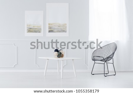 Metal wire net chair and a small, white, wooden coffee table in a bright and luxurious living room interior