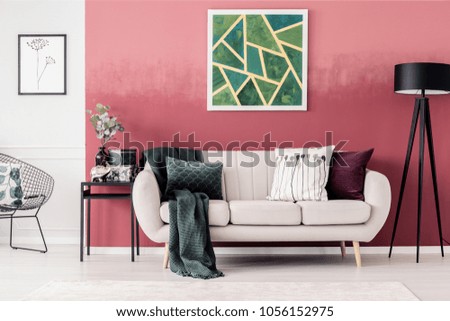 White sofa with blanket and pillows and green, geometric painting on red wall in living room interior