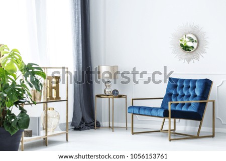 Navy blue armchair next to table with gold lamp in elegant living room interior with mirror