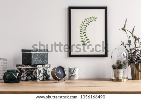 Patterned boxes and cactus standing on a wooden table in a room with poster on the wall