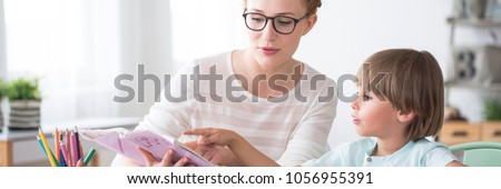 Panorama of kid learning to read during extracurricular activities with a tutor