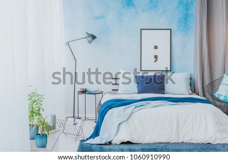 Romantic bedroom interior with blue accents, poster, lamp and watercolor paint on the wall