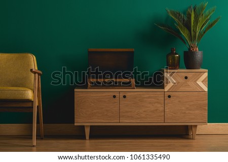 Close-up of a retro wooden dresser with a hipster record player in a minimalist dark green living room interior