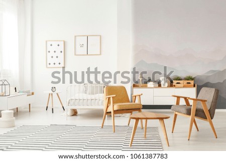 Grey and yellow armchair in open space interior with white child\'s bed against the wall with posters