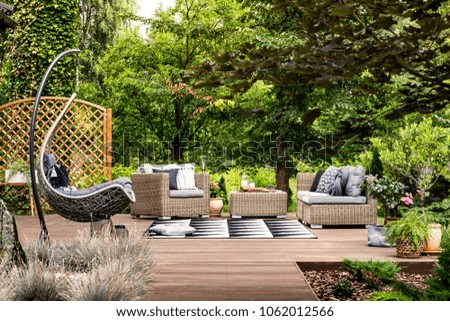 Hanging chair and geometric carpet on wooden patio with rattan garden furniture
