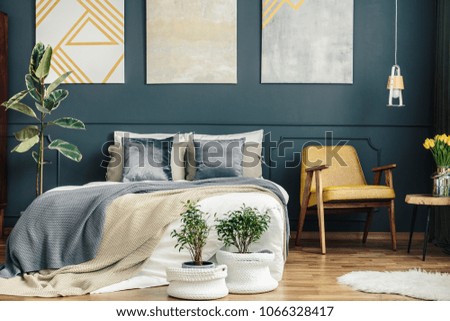 Vintage bedroom interior with retro chair, blue and grey blankets, cushions, plants, white carpet and modern paintings