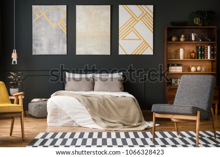 Modern bedroom interior with big bed, grey and white carpet, chairs, paintings, lamp and bookcase with books and decorations