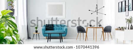 Two coffee cups on a wooden table in white living room interior with blue couch and silver painting on the wall