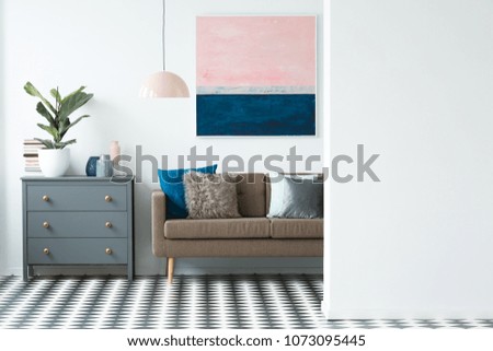 Plant on black cabinet next to a brown sofa in colorful living room interior with pastel painting
