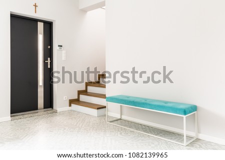 Black front door, stairs and a turquoise upholstered bench seat in a white entrance hall interior
