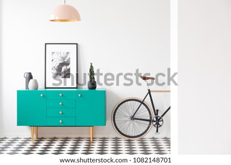 Blue cabinet with plant and poster in modern living room interior with bicycle and pink lamp
